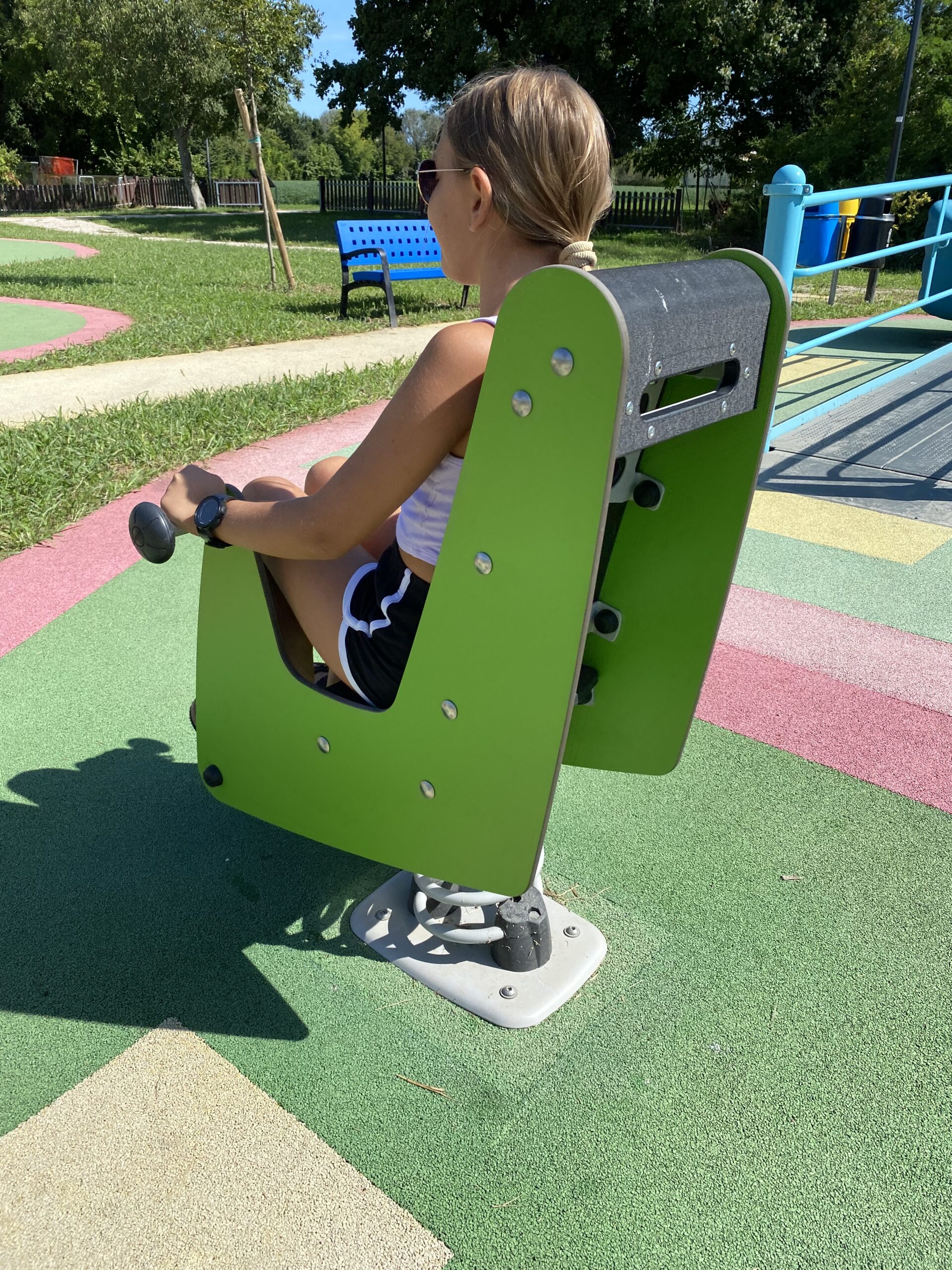 una bambina si dondola seduta dentro la giostra verde a molla del parco