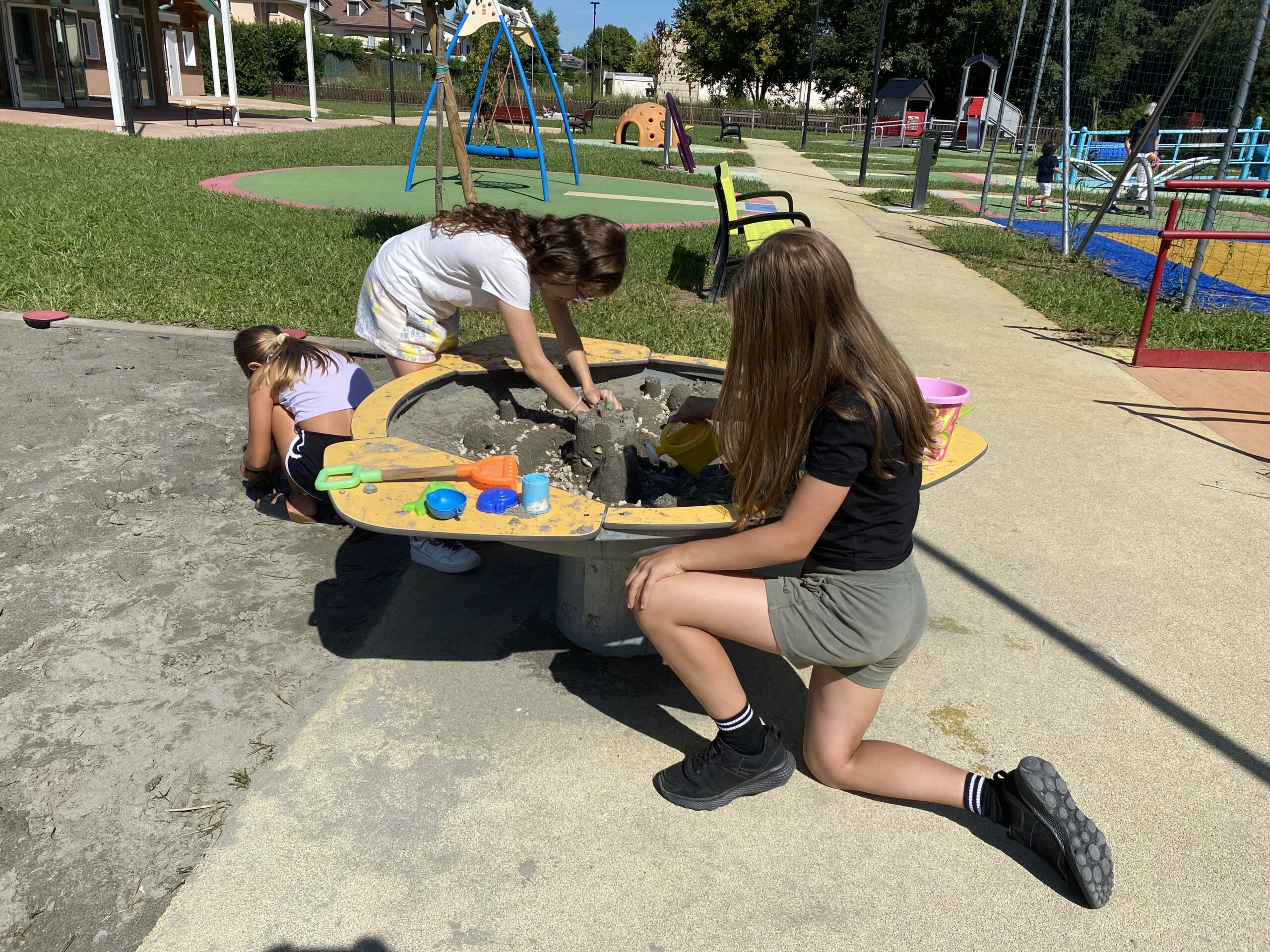 Tre bambine giocano con la sabbia su due sabbiere: una rialzata e l'altra a terra